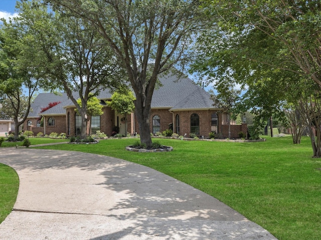 english style home with brick siding, a shingled roof, and a front yard