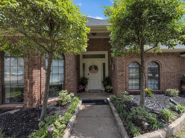view of exterior entry featuring brick siding and a shingled roof
