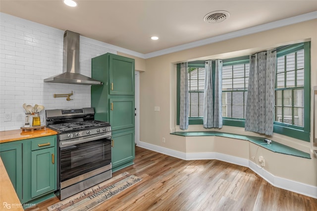 kitchen with stainless steel range with gas cooktop, green cabinetry, wall chimney range hood, backsplash, and baseboards