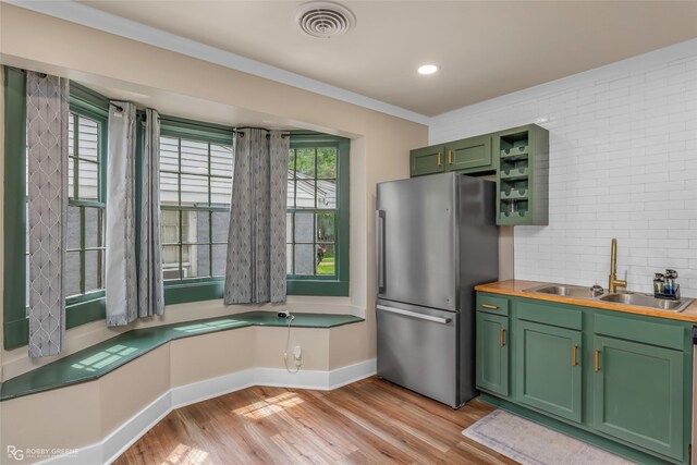 kitchen featuring freestanding refrigerator, green cabinetry, a sink, light wood-style floors, and baseboards