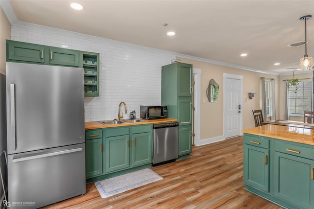 kitchen with appliances with stainless steel finishes, a sink, wooden counters, green cabinetry, and backsplash