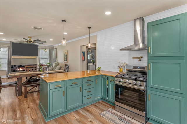 kitchen with stainless steel gas range oven, wall chimney range hood, plenty of natural light, a peninsula, and crown molding