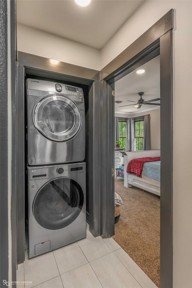 laundry area featuring stacked washer / drying machine, tile patterned flooring, ceiling fan, and carpet flooring