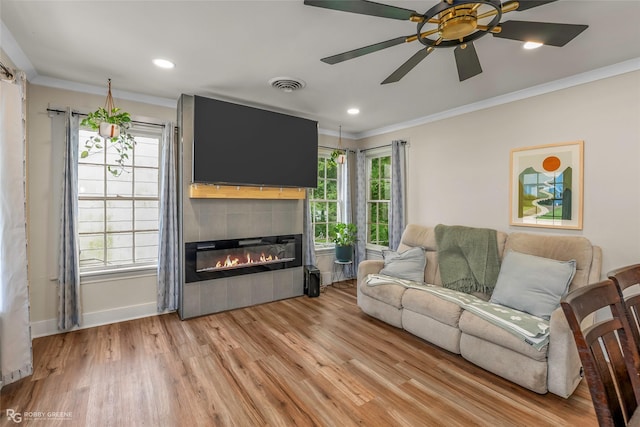 living area featuring ornamental molding, light wood-type flooring, a fireplace, a ceiling fan, and baseboards