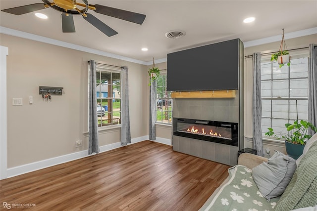 living room with ornamental molding, wood finished floors, baseboards, a tile fireplace, and ceiling fan