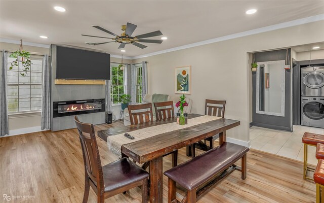 dining room featuring estacked washer and dryer, ornamental molding, a ceiling fan, light wood finished floors, and a fireplace