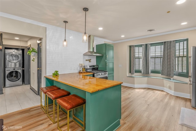 kitchen with appliances with stainless steel finishes, stacked washer / dryer, wall chimney exhaust hood, green cabinets, and decorative backsplash