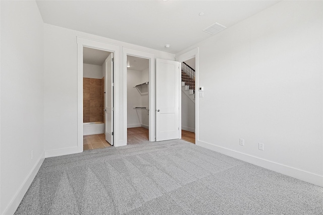 unfurnished bedroom with connected bathroom, visible vents, baseboards, carpet floors, and a walk in closet