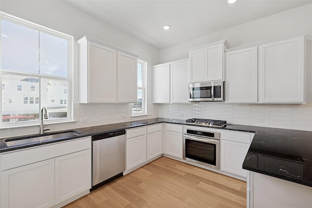 kitchen featuring dark stone countertops, light wood-style flooring, white cabinets, a sink, and stainless steel appliances