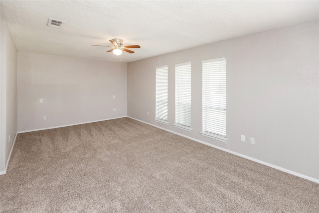 carpeted spare room featuring a textured ceiling, visible vents, ceiling fan, and baseboards