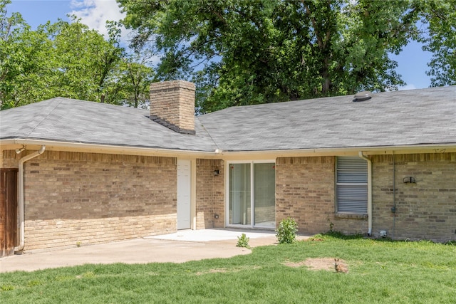 back of house with a shingled roof, a patio area, brick siding, a lawn, and a chimney