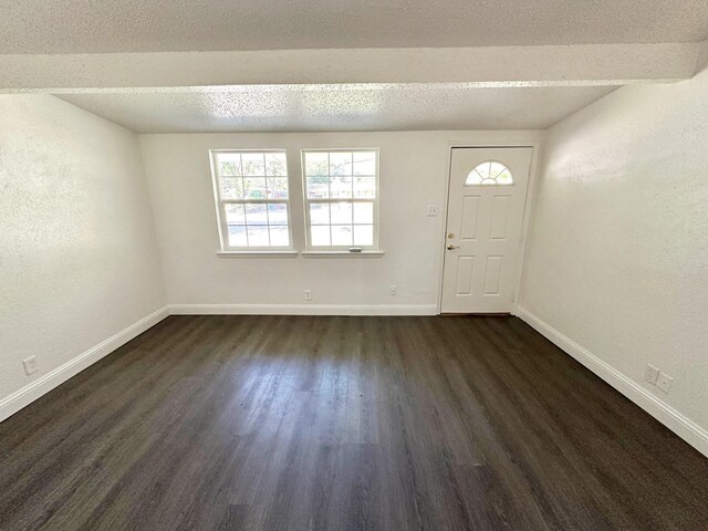 foyer featuring dark wood-type flooring, a textured wall, a textured ceiling, and baseboards