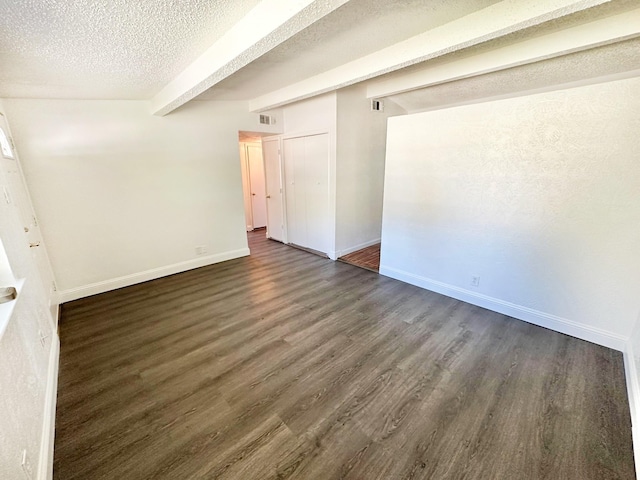 spare room featuring beam ceiling, a textured ceiling, dark wood finished floors, and baseboards