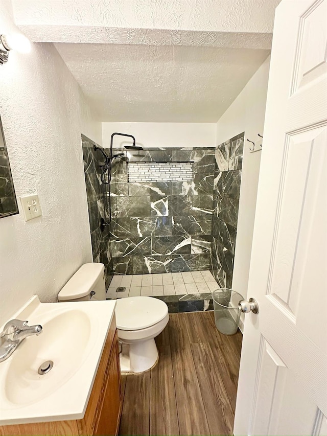 full bath featuring tiled shower, toilet, a textured wall, a textured ceiling, and wood finished floors