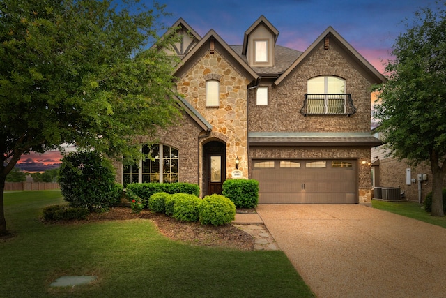 view of front of home featuring driveway, central AC, a yard, an attached garage, and stone siding