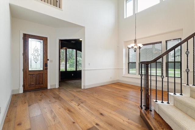 entryway featuring light wood-type flooring, stairs, a chandelier, and a towering ceiling