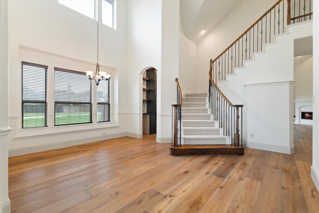 entrance foyer with a warm lit fireplace, a chandelier, stairs, a towering ceiling, and hardwood / wood-style flooring