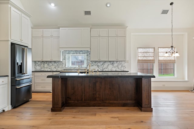 kitchen with stainless steel fridge, light wood finished floors, visible vents, and dark countertops