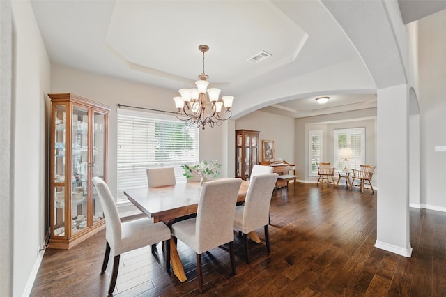 dining space featuring dark wood-style flooring, arched walkways, a chandelier, and a raised ceiling