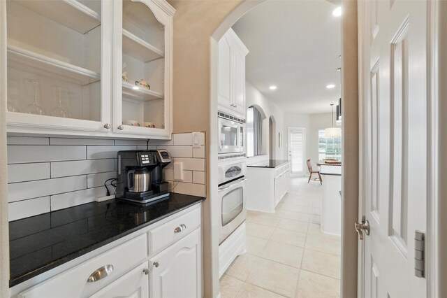 kitchen with glass insert cabinets, white cabinetry, arched walkways, appliances with stainless steel finishes, and light tile patterned floors
