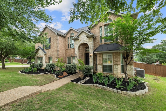 traditional-style home with fence, central AC, stone siding, a front yard, and a standing seam roof