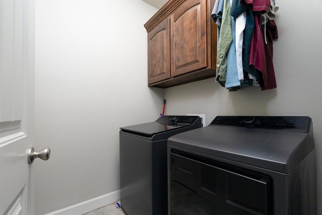 clothes washing area featuring baseboards, cabinet space, and washing machine and dryer
