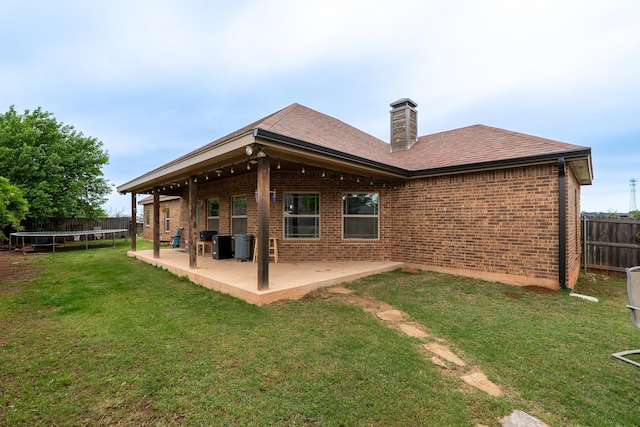 back of property featuring a trampoline, a chimney, a patio area, fence, and brick siding