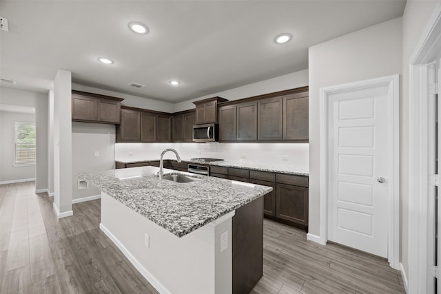 kitchen with light stone countertops, stainless steel appliances, dark brown cabinets, light wood finished floors, and a sink