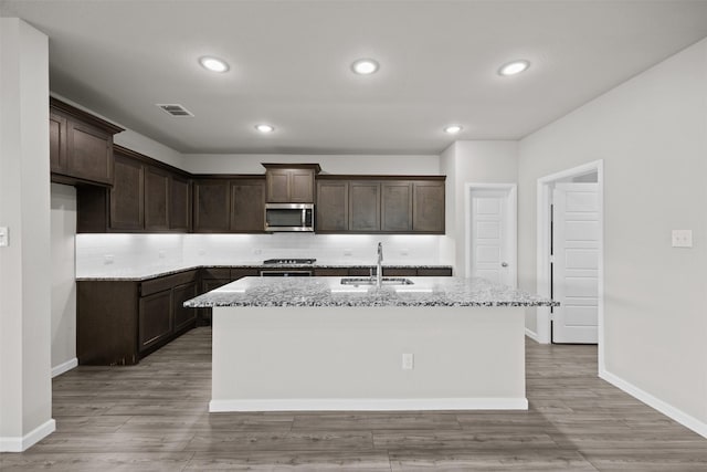 kitchen with light stone countertops, dark brown cabinetry, stainless steel microwave, a sink, and visible vents