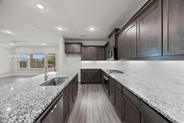 kitchen featuring light stone countertops, a sink, light wood-style flooring, and stainless steel appliances