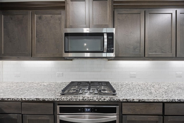 kitchen with light stone countertops, dark brown cabinets, appliances with stainless steel finishes, and tasteful backsplash