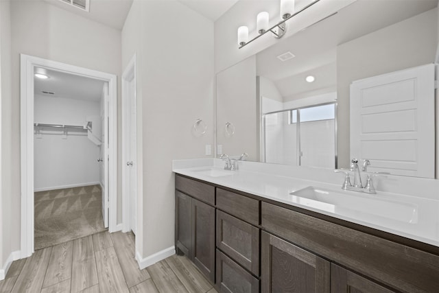 bathroom featuring a walk in closet, a shower stall, double vanity, and a sink