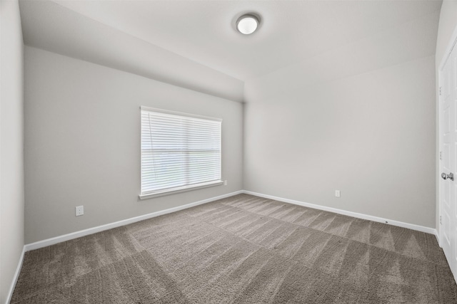 empty room featuring lofted ceiling, carpet floors, and baseboards