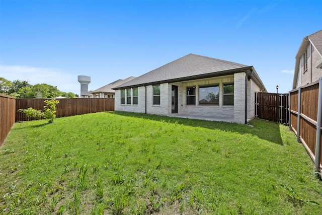 back of property with roof with shingles, a yard, brick siding, and a fenced backyard