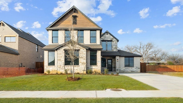 view of front of house featuring fence, roof with shingles, a front yard, and stone siding