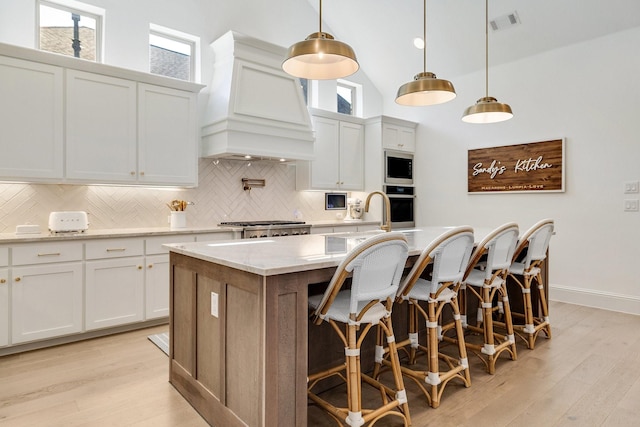 kitchen with a center island with sink, custom exhaust hood, backsplash, a towering ceiling, and stainless steel oven