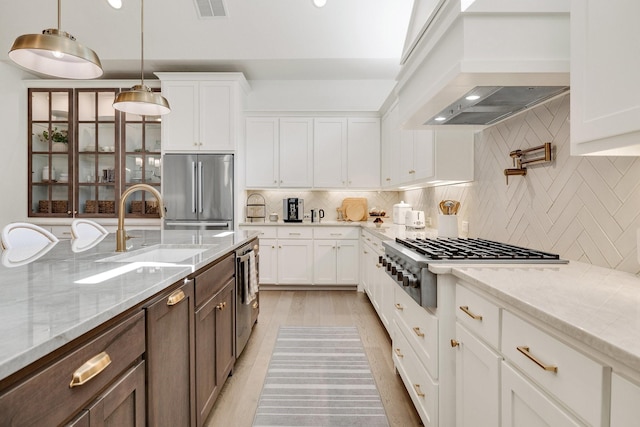 kitchen featuring a sink, stainless steel appliances, custom range hood, visible vents, and white cabinetry