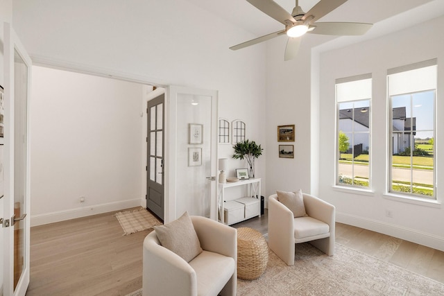 living area with baseboards, ceiling fan, and light wood finished floors