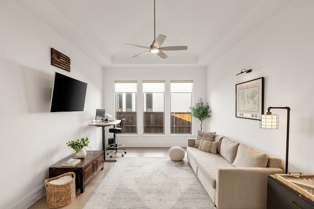 living area with ceiling fan and a raised ceiling