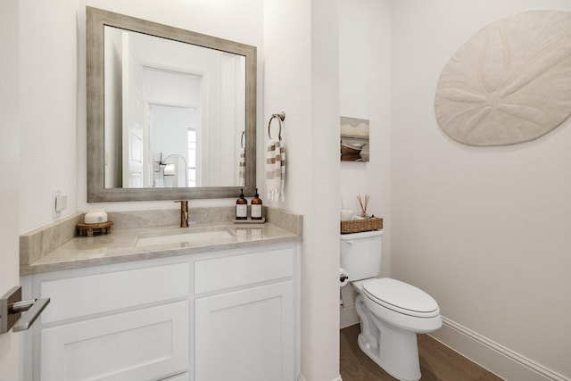 half bathroom with toilet, vanity, wood finished floors, and baseboards