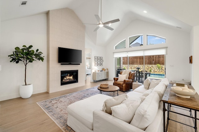 living room featuring a large fireplace, ceiling fan, high vaulted ceiling, visible vents, and wood finished floors