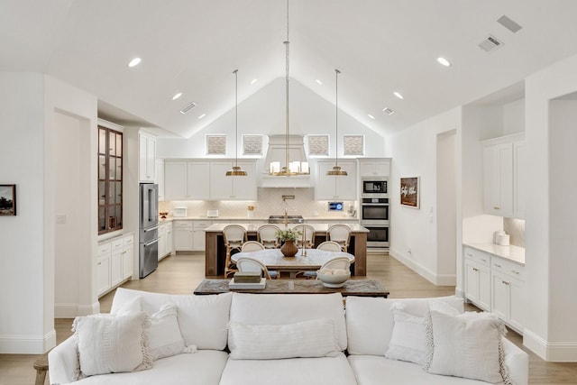 living room featuring visible vents, light wood-type flooring, and high vaulted ceiling