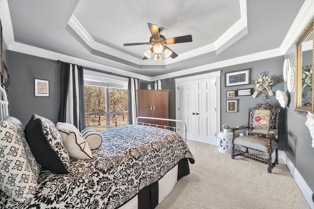 bedroom with crown molding, light colored carpet, ceiling fan, a tray ceiling, and a closet