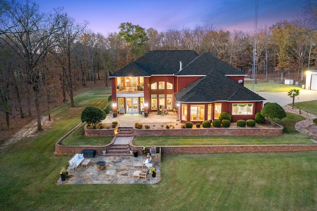 back of house at dusk featuring a balcony, a patio area, a lawn, roof with shingles, and french doors