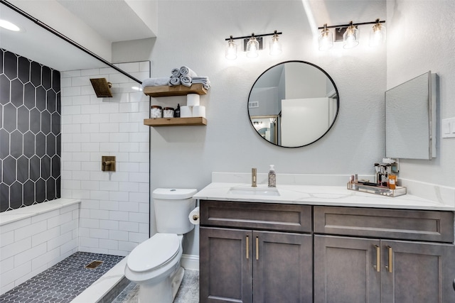 full bathroom with toilet, tiled shower, and vanity