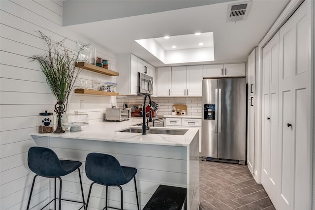 kitchen with decorative backsplash, open shelves, appliances with stainless steel finishes, visible vents, and a peninsula