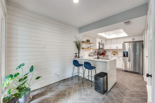 kitchen with a kitchen breakfast bar, appliances with stainless steel finishes, a raised ceiling, visible vents, and a peninsula
