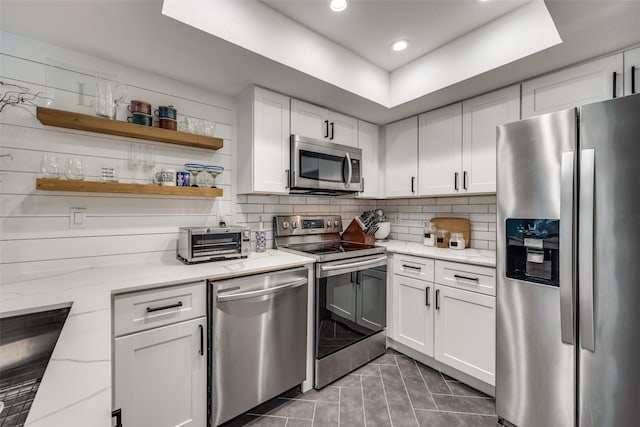 kitchen featuring tasteful backsplash, light stone counters, a toaster, stainless steel appliances, and white cabinetry