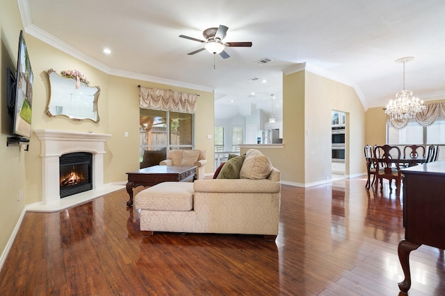 living area featuring a warm lit fireplace, ornamental molding, ceiling fan with notable chandelier, visible vents, and dark wood-type flooring