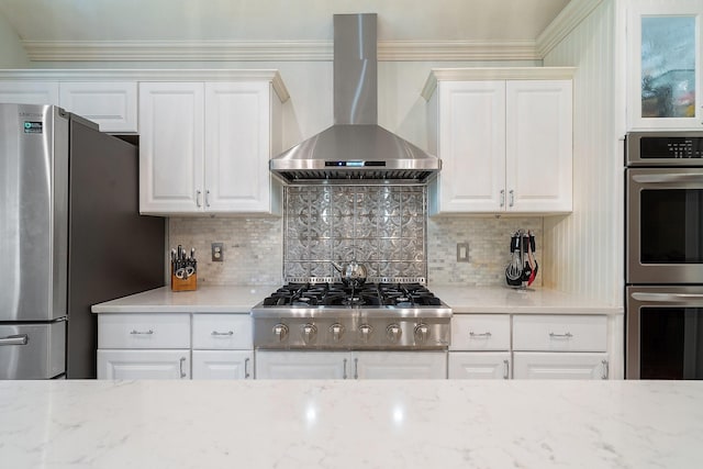 kitchen featuring light stone counters, white cabinetry, tasteful backsplash, appliances with stainless steel finishes, and wall chimney exhaust hood